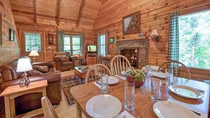 Interior de una cabaña de madera con comedor, sala de estar y chimenea.