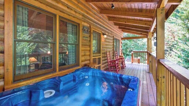 Una cabaña de madera con jacuzzi en el porche, ventanas amplias y una terraza.