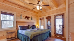 A wooden cabin bedroom with a bed, a ceiling fan, a window, and a door. - Back to Nature by Jackson Mountain Rentals (Gatlinburg)