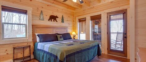 A wooden cabin bedroom with a bed, a ceiling fan, a window, and a door.