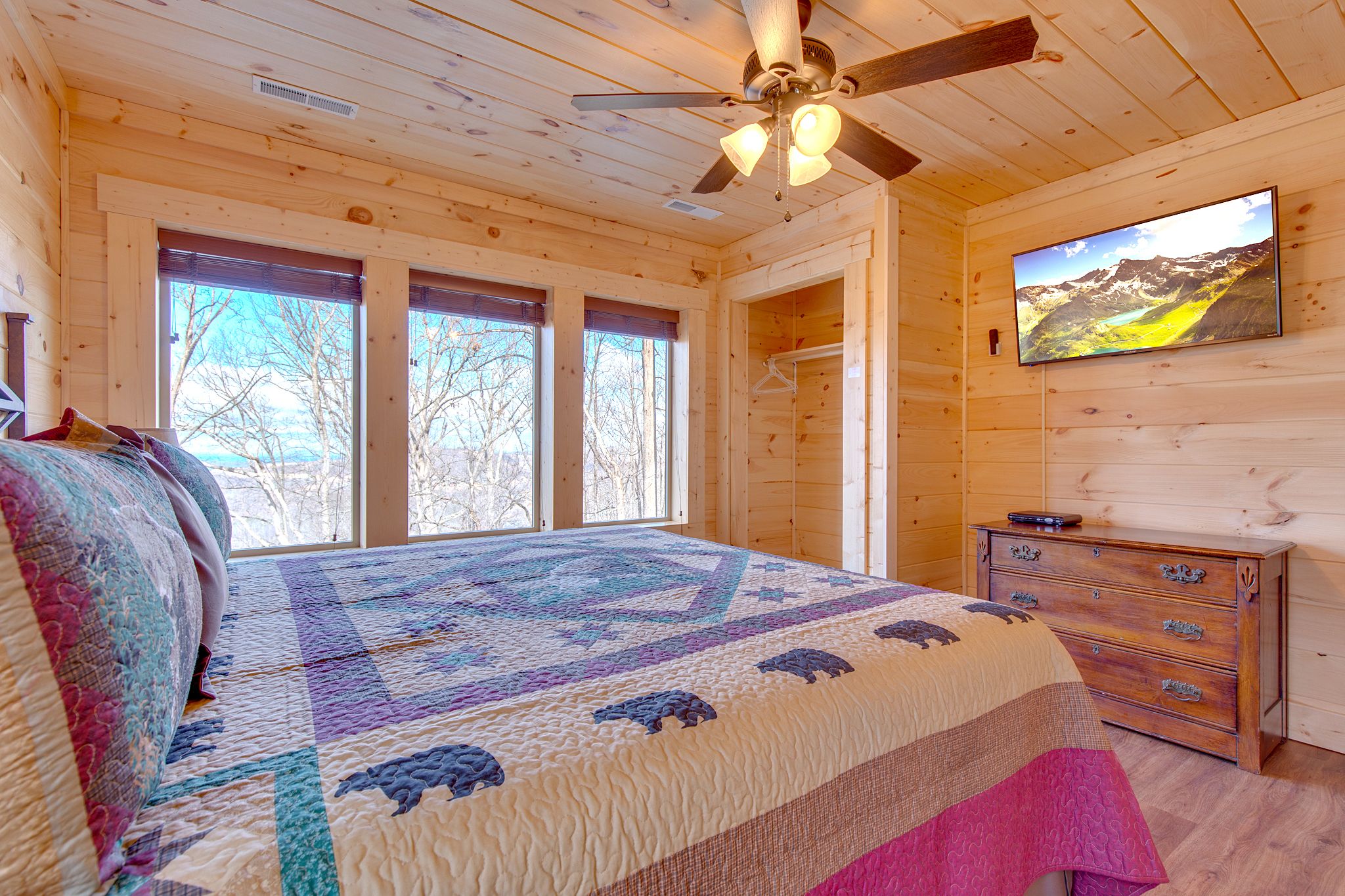 A wooden cabin bedroom with a bed, dresser, and a TV on the wall.