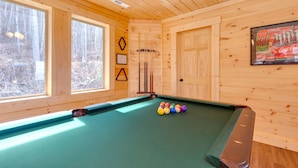 A pool table with balls in a wooden room with large windows and a door. - Back to Nature by Jackson Mountain Rentals (Gatlinburg)
