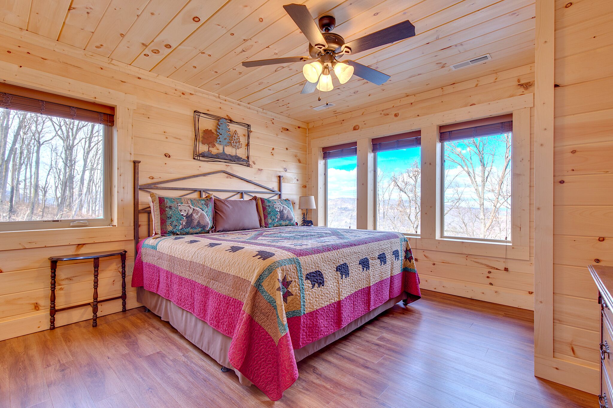 Une chambre dans une cabane en bois, avec un lit, des fenêtres et un ventilateur de plafond.