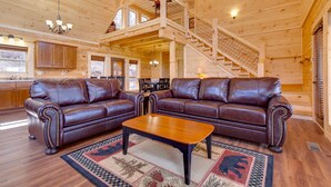 A spacious living room with a wooden ceiling, a brown leather sectional sofa, a wooden coffee table, and a staircase leading to an upper level. - Back to Nature by Jackson Mountain Rentals (Gatlinburg)