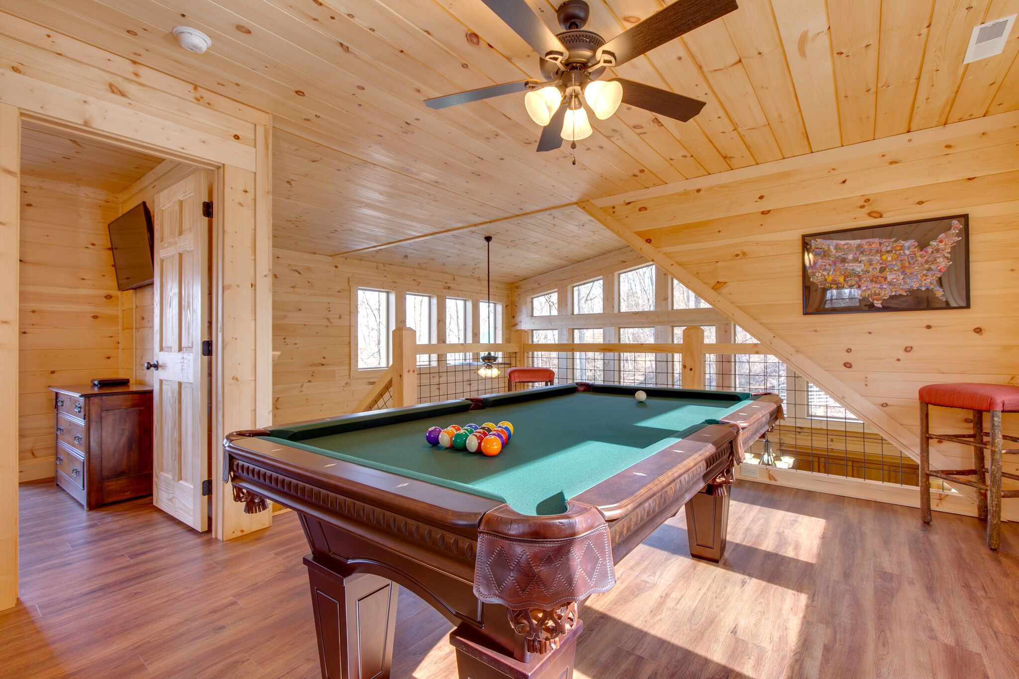 A wooden interior with a pool table, a ceiling fan, and a window with a view of the outdoors.