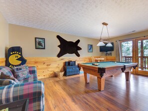 A room with a pool table, a sofa, a bear head wall decoration, and a Super Mario poster. - Cub's Corner by Jackson Mountain Rentals (Gatlinburg)