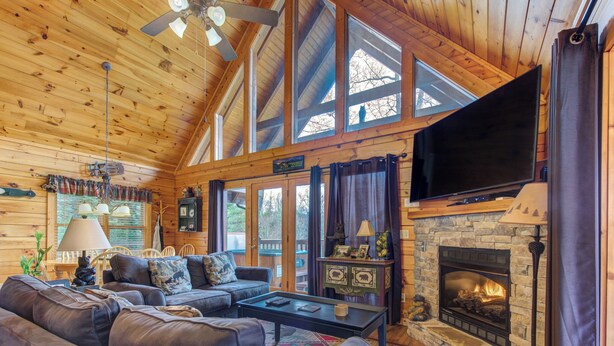 Interior acogedor de una cabaña con chimenea, sofás de cuero, un televisor de pantalla plana y un ventanal con vistas al exterior.