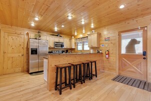 Cocina estilo cabaña de madera con refrigerador, microondas y taburetes de bar.