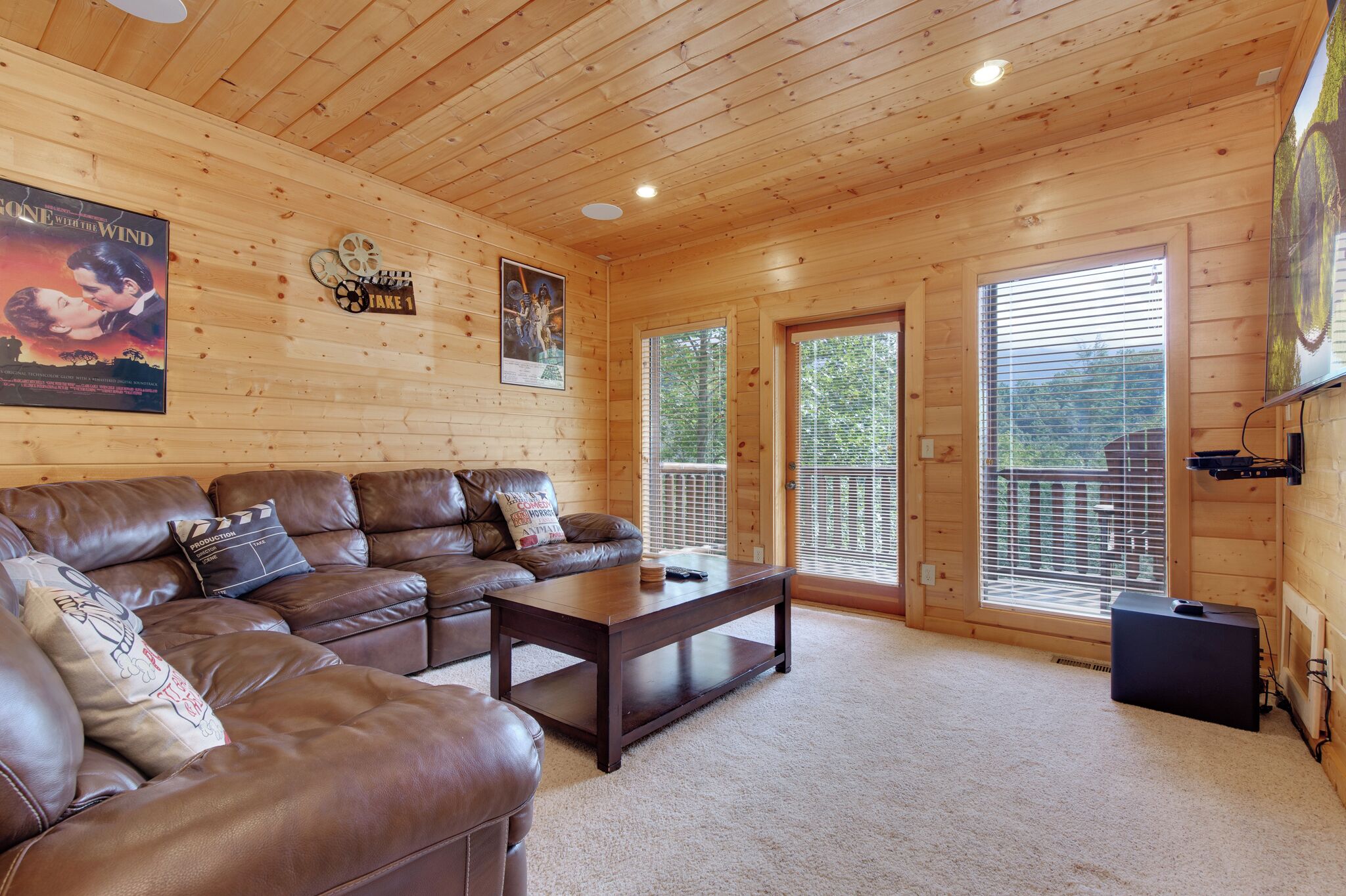 A cozy living room with a brown leather sectional sofa, a dark wooden coffee table, and a large poster on the wall.