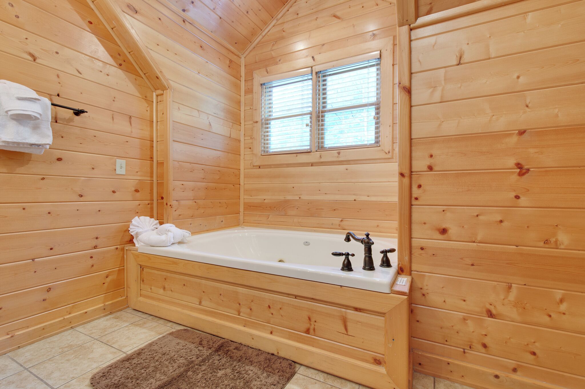 A wooden cabin bathroom with a bathtub, a window, and a towel rack.