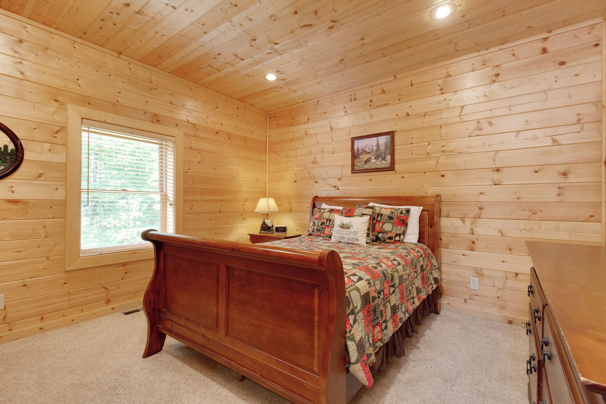 Un dormitorio con paneles de madera, una cama, una mesita de noche, una lámpara y una ventana.