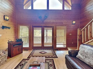 L’intérieur d’une cabane en rondins, avec un plancher en bois, un canapé, une table basse, une cheminée et un balcon doté de balustrades en bois.