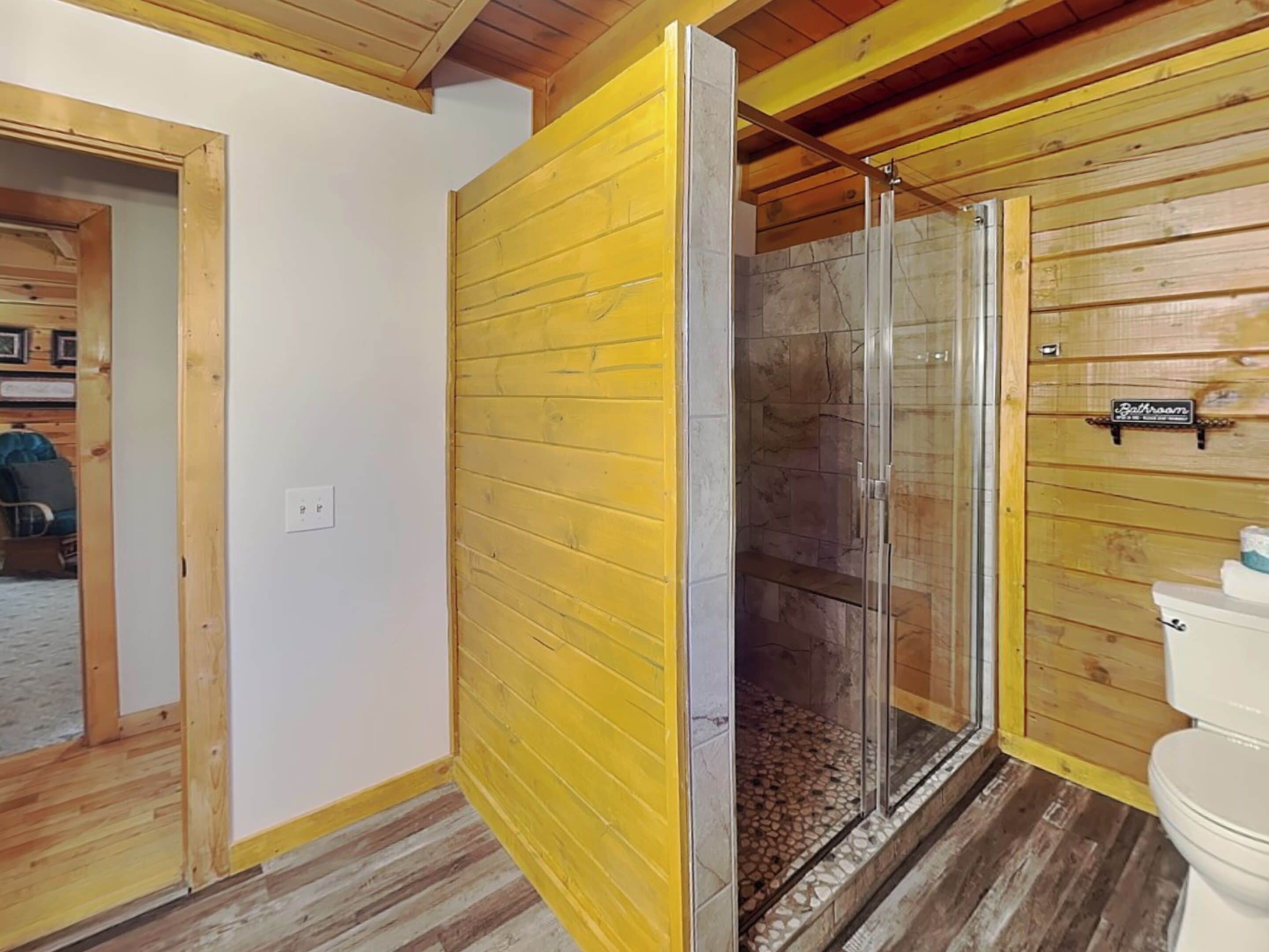 A bathroom with wooden walls, a glass shower enclosure, and a toilet.