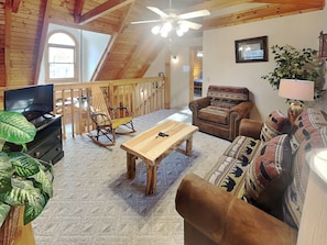 A cozy living room with a wooden ceiling, a television, a rocking chair, a sofa, and a coffee table.