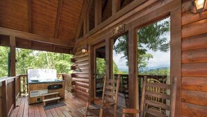 Um deck de madeira com hidromassagem, cadeiras de madeira e vista para as montanhas.