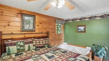Een slaapkamer met een houten hoofdbord, een gewatteerde sprei, een plafondventilator en een raam met uitzicht op bomen.