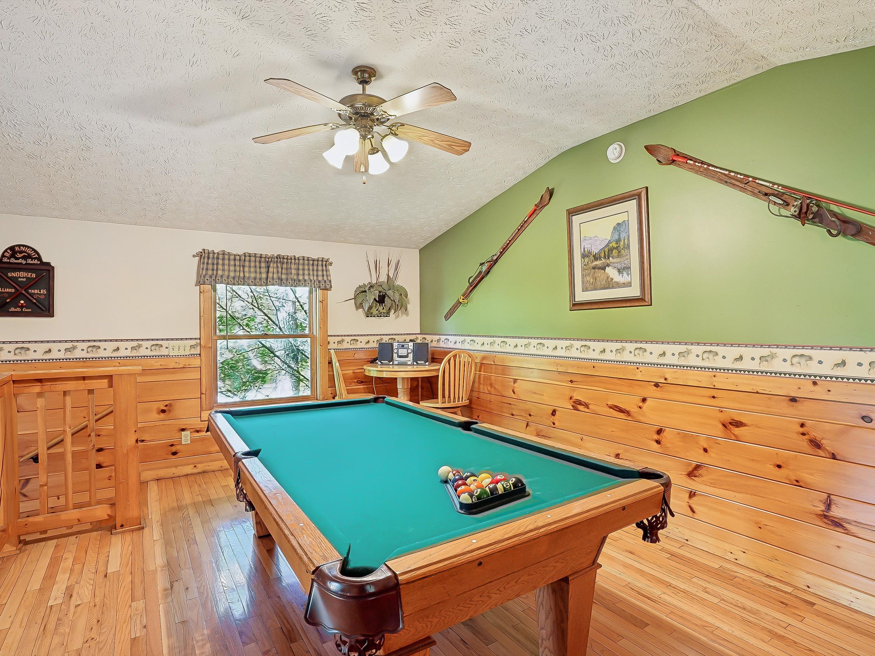A pool table with a green felt surface, wooden benches, and a ceiling fan.