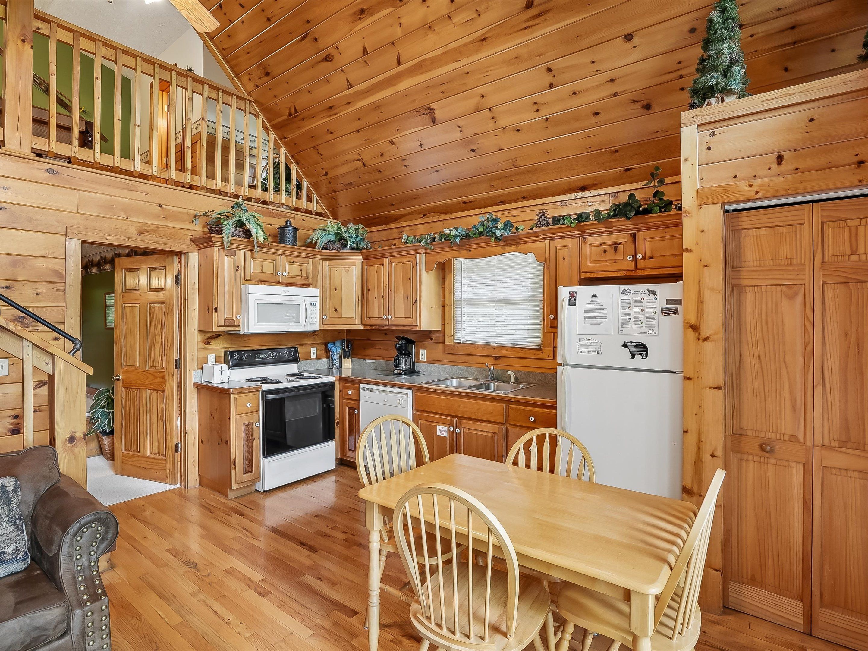A wooden cabin interior with a kitchen, dining area, and staircase.