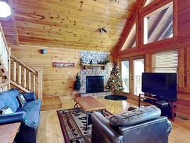 Un interior de cabaña acogedor con detalles de madera, una chimenea, un árbol de Navidad, un televisor y un sofá.
