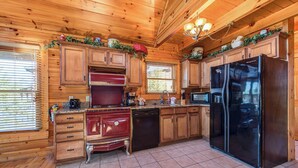 A wooden cabin kitchen with a red stove, black dishwasher, and a large black refrigerator. - Cloud Dancer by Jackson Mountain Rentals (Gatlinburg)
