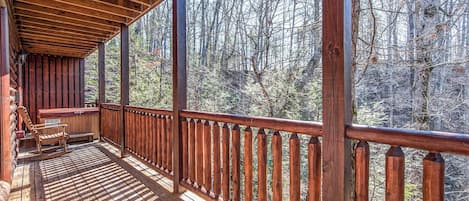 A wooden deck with a railing, a bench, and a hot tub.