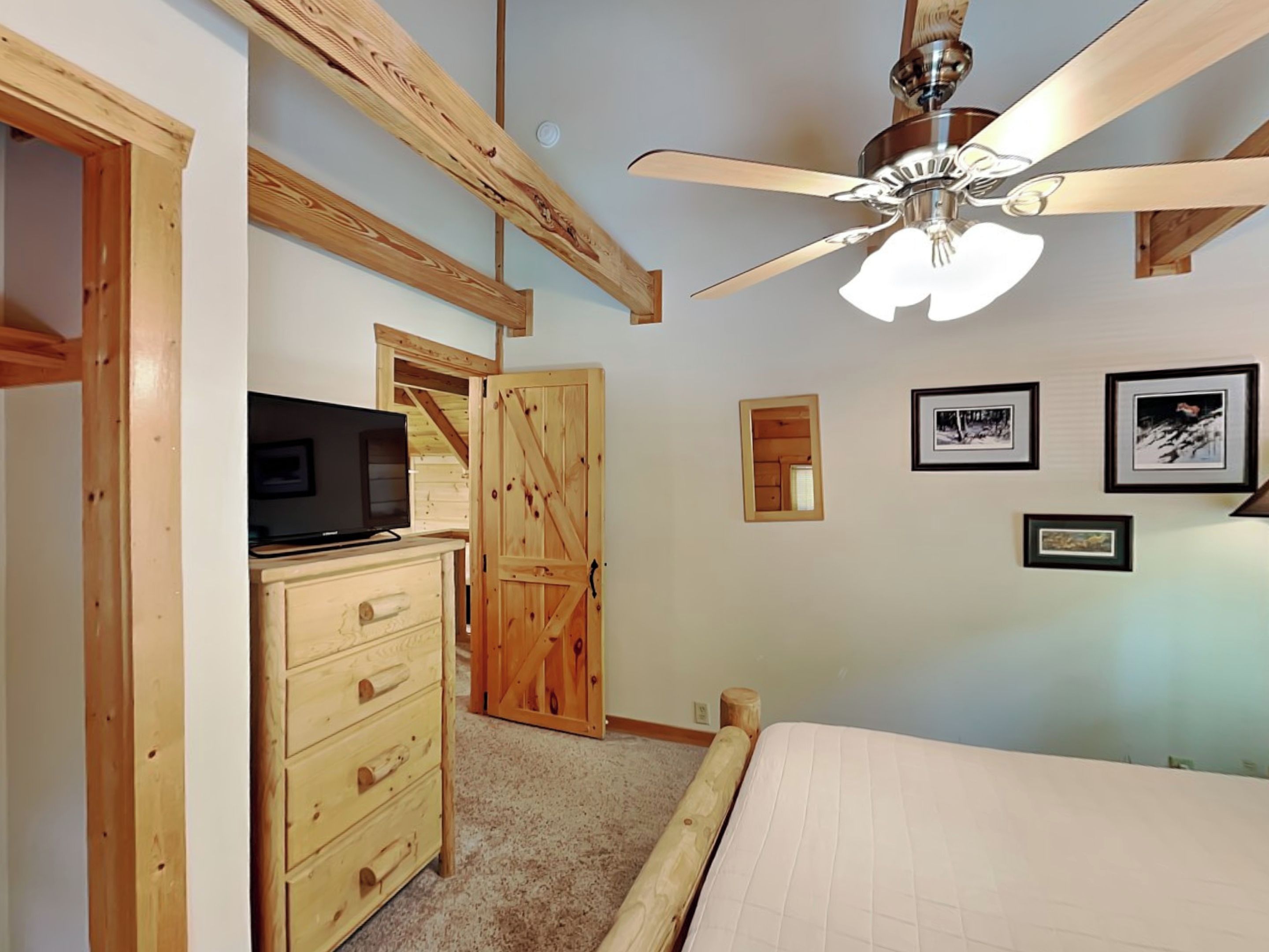 Ein Schlafzimmer mit einem Bett, einem Deckenventilator, einer hölzernen Kommode, einem Fernseher und gerahmten Bildern an der Wand.
