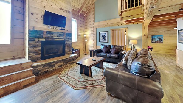 A cozy log cabin interior with a stone fireplace, leather sofas, and a wooden ceiling. - Big Bear 2 (Gatlinburg)