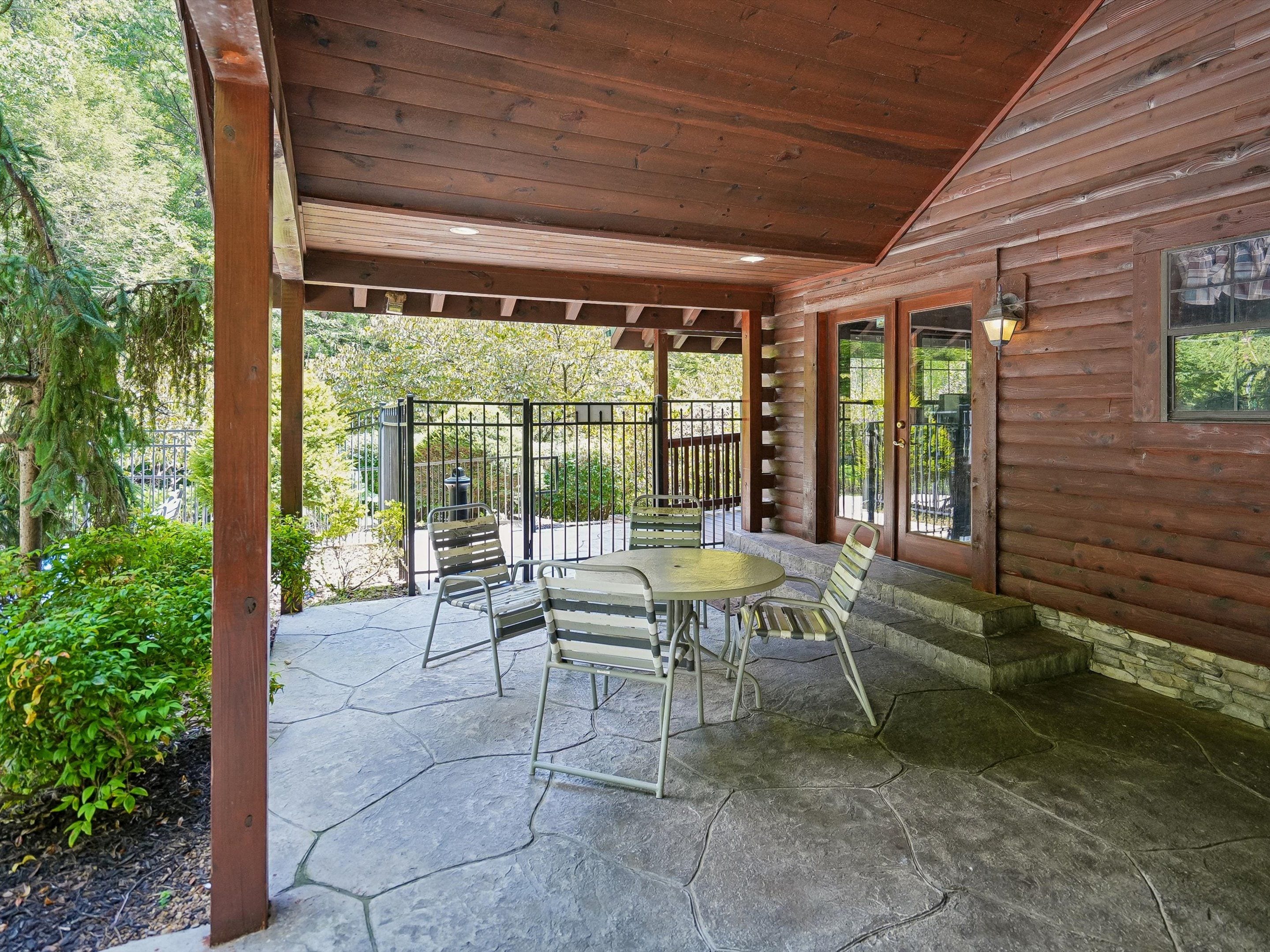 A covered patio with a stone floor, wooden railing, and a table with chairs.