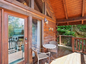 A wooden deck with a glass door, wicker chairs, and a small table.