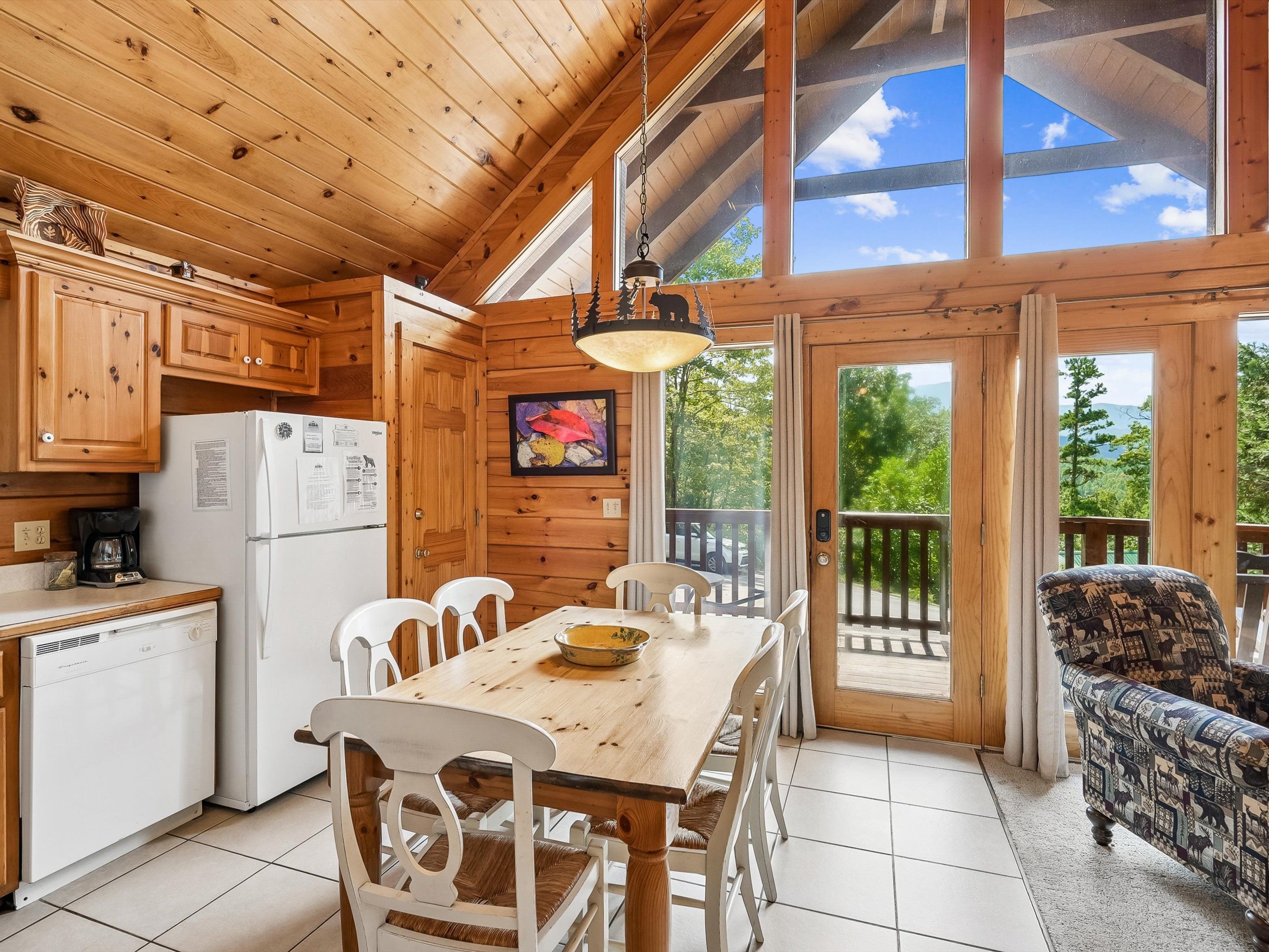 A wooden cabin interior with a dining table, chairs, a refrigerator, and a sofa.