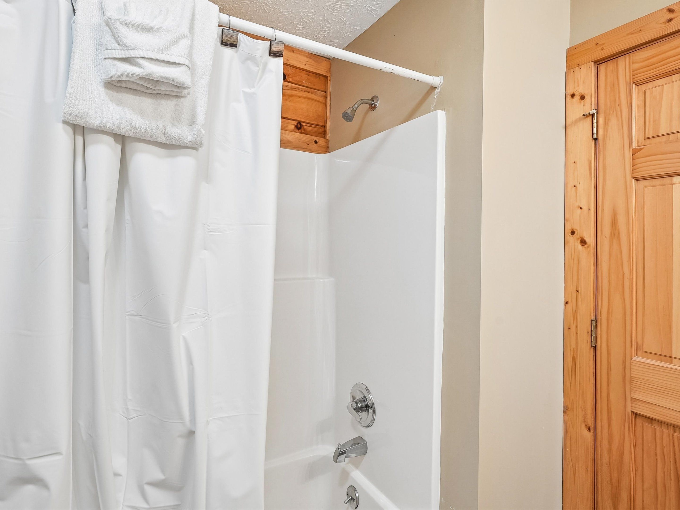 Una doccia con tenda bianca, una porta di legno e una vasca da bagno bianca.