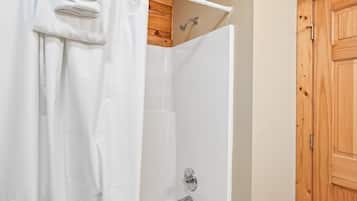 Une douche avec un rideau blanc, une porte en bois et une baignoire blanche.
