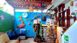 Una habitación con pared azul, un mostrador de recepción de madera y una pared de piedra. Hay un sofá, una silla y una pequeña mesa.