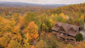 A wooden cabin with a balcony, surrounded by a forest with autumn foliage. - Dreamscapes by Jackson Mountain Rentals (Gatlinburg)