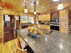Una cocina moderna con encimeras de granito, electrodomésticos de acero inoxidable, armarios de madera y una isla central con un jarrón de flores.