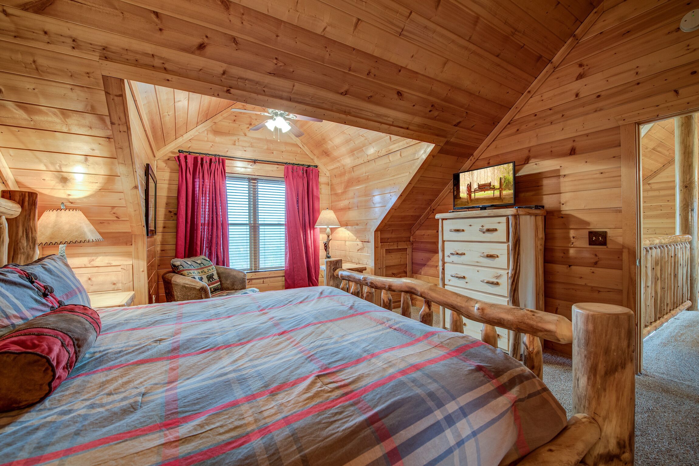 A cozy wooden cabin bedroom with a bed, a dresser, and a window with curtains.
