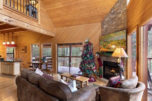 A cozy cabin interior with a wooden interior, a fireplace, a Christmas tree, and a dining area. - Dreams & Streams by Jackson Mountain Rentals (Gatlinburg)