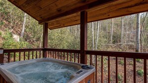 A hot tub under a wooden deck with a view of a forest. - Dreams & Streams by Jackson Mountain Rentals (Gatlinburg)