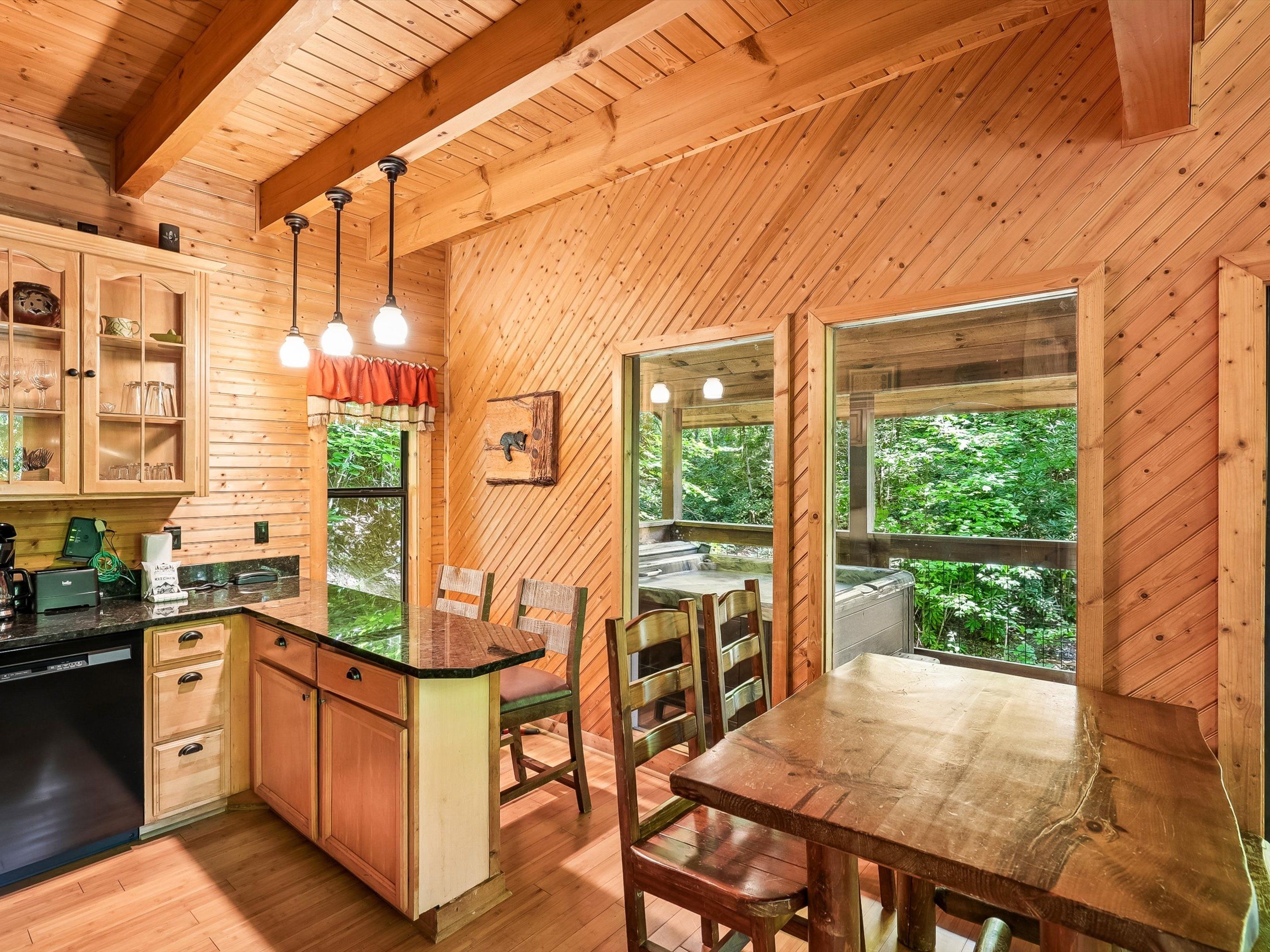 A wooden cabin interior with a kitchen, dining area, and large windows.