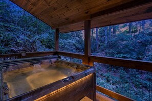 A hot tub with a wooden deck and a view of a forested area. - Dreams & Streams by Jackson Mountain Rentals (Gatlinburg)