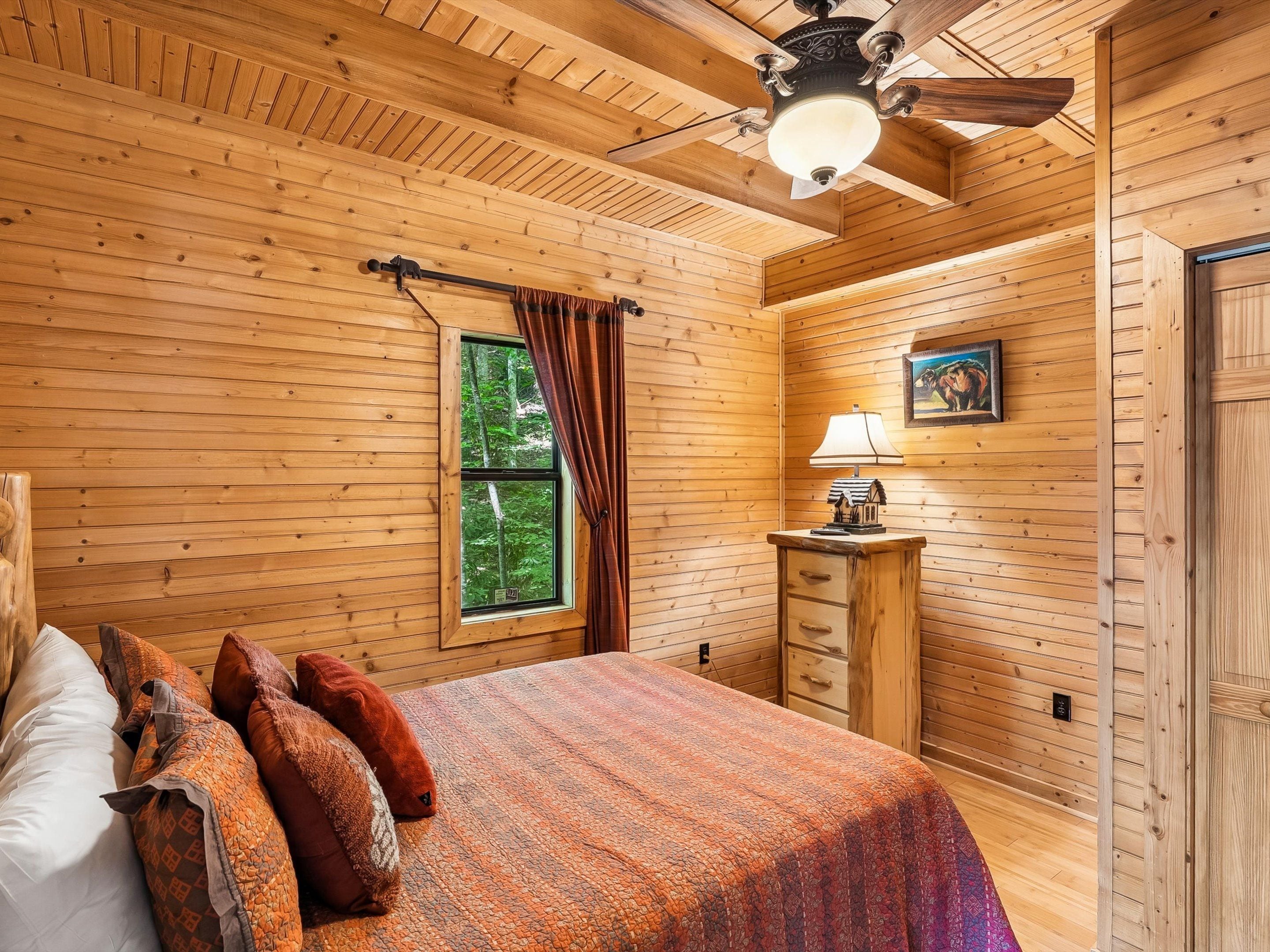 Un dormitorio con paneles de madera, una cama, una mesita de noche, una lámpara y un ventanal con cortinas.