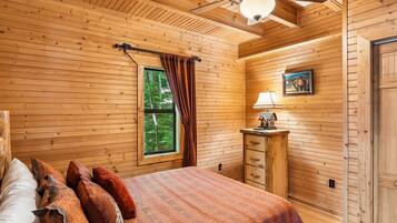 Un dormitorio con paneles de madera, una cama, una mesita de noche, una lámpara y un ventanal con cortinas.