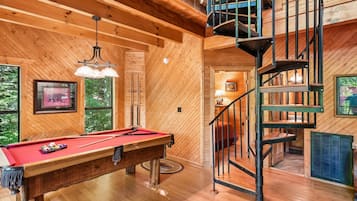 A wooden interior with a pool table, a spiral staircase, and a framed picture on the wall.