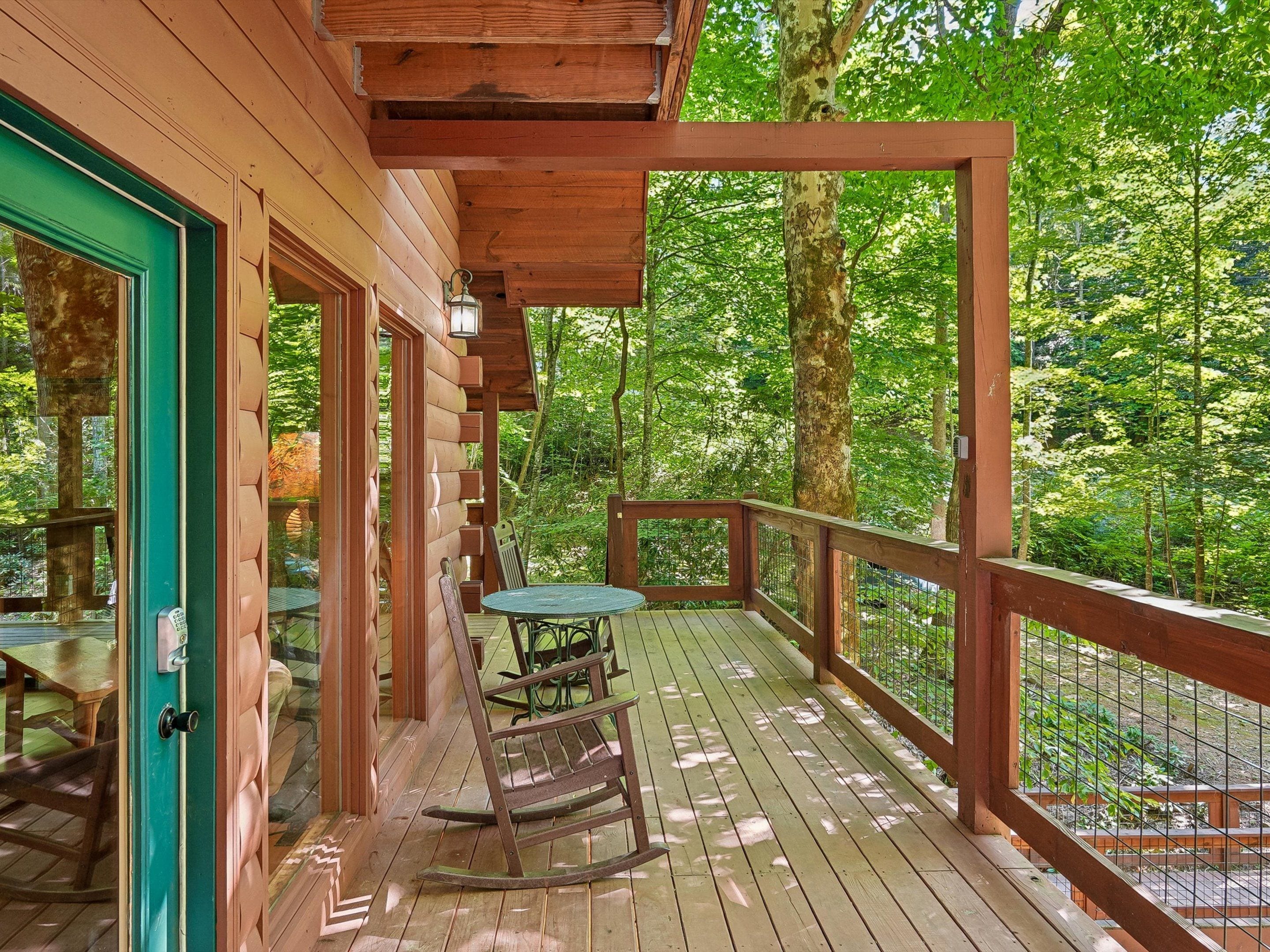 A wooden deck with a table and chairs, surrounded by a wooden railing, overlooking a forested area.