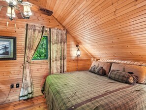 Un dormitori d'una cabana de fusta acollidora, amb un llit, cortines, una làmpada penjada a la paret i un quadre amb marc.