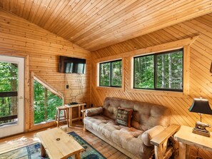 A cozy cabin interior with a wooden ceiling, a sofa, a table, and a TV mounted on the wall. - Dreams & Streams by Jackson Mountain Rentals (Gatlinburg)