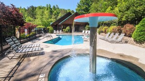 A swimming pool with a water feature, lounge chairs, and a building in the background. - Eagles Point Lodge by Jackson Mountain Rentals (Gatlinburg)