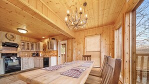 A wooden interior with a large dining table, wooden cabinets, a chandelier, and large windows. - Eden's View by Jackson Mountain Rentals (Gatlinburg)