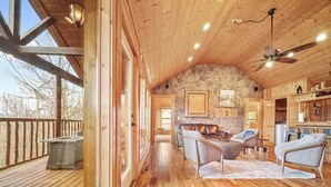 A spacious wooden cabin with a stone wall, a dining area, and a seating area with a fireplace. - Eden's View by Jackson Mountain Rentals (Gatlinburg)