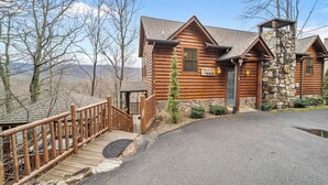 A log cabin with a stone chimney, a wooden deck, and a sign reading "Eden's View". - Eden's View by Jackson Mountain Rentals (Gatlinburg)